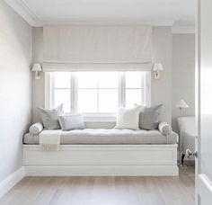 a window seat in the corner of a room with white walls and wood flooring