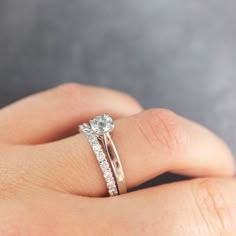 a woman's hand with a diamond ring on top of her finger and the other hand holding an engagement ring