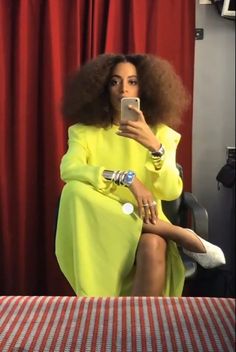 a woman in a yellow dress is sitting on a chair and looking at her cell phone