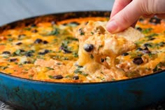 a hand dipping a tortilla chip into a bowl of quesadilla