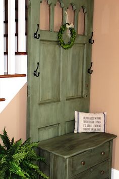 a green door sitting next to a plant and a wooden bench with a pillow on it