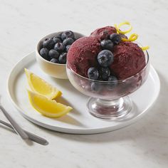 two bowls of ice cream with blueberries and lemon wedges on a white plate