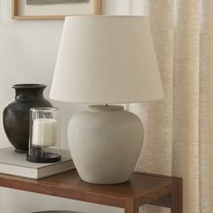 a white vase sitting on top of a table next to a lamp