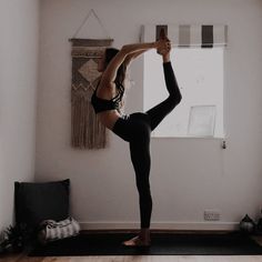 a woman is doing yoga in front of a window and holding her leg up to the side