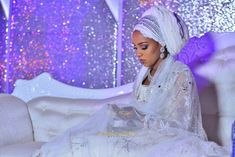 a woman sitting on top of a white couch in front of a purple and silver wall