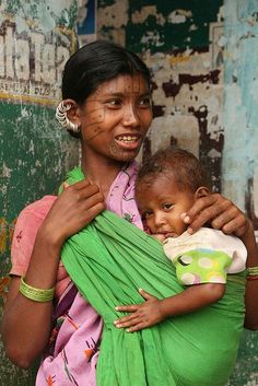 a woman holding a baby in her arms and wearing a green wrap around her neck