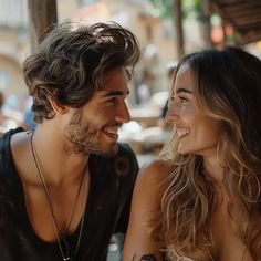 a man and woman sitting next to each other in front of a window smiling at each other