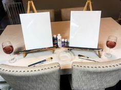 two empty canvases sitting on top of a table next to wine glasses and pens