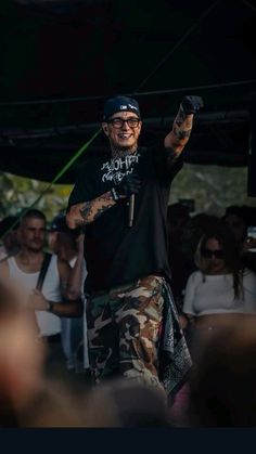 a man in black shirt and camo pants on stage with arms raised to the side