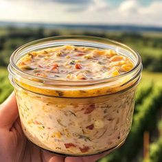 a hand holding a glass jar filled with food on top of a lush green field