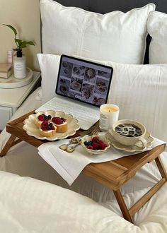 a laptop computer sitting on top of a bed next to two plates of food and drinks