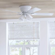 a white ceiling fan hanging from the ceiling in front of two windows with blinds on them