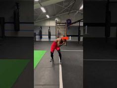 a man in red shirt and black pants holding an orange frisbee while standing next to a punching bag