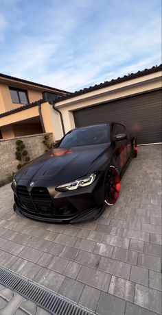 a black sports car parked in front of a house with red rims on it