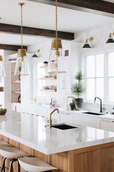 a kitchen with white counter tops and gold pendant lights hanging from the ceiling over the island