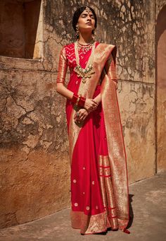 a woman in a red and gold sari standing next to a wall with her eyes closed