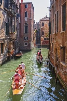 two gondolas in the middle of a canal with buildings on both sides and people rowing them