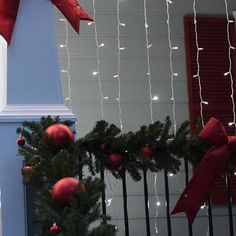 a christmas tree with red balls and lights on it next to a white pillar in front of a house