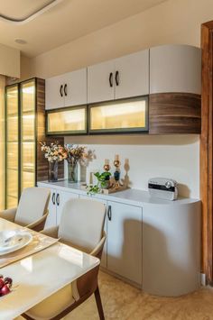 a dining room table and chairs with white cupboards on the wall in front of them