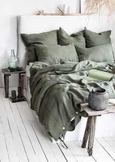 a bed with green sheets and pillows in a room next to a small table on the floor