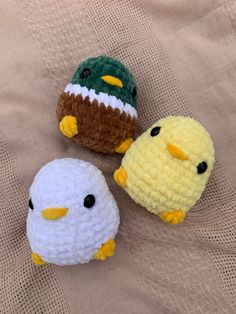 three small crocheted birds sitting next to each other on a cloth covered surface