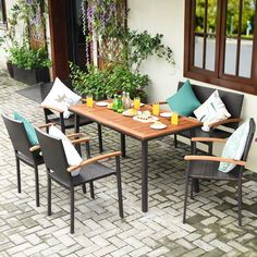 an outdoor dining table with chairs and pillows on the outside brick patio, surrounded by potted plants