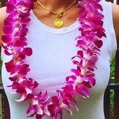 a woman wearing a necklace made out of pink flowers with a gold disc on it