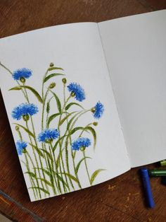 an open notebook with blue flowers and green stems painted on the pages, next to crayons