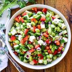 a white bowl filled with cucumber, tomatoes and feta cheese on top of a wooden table