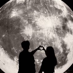 two people standing in front of the moon making a heart shape with their hands, black and white photograph