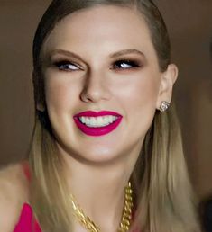 a woman with long blonde hair and bright red lipstick is smiling at the camera while wearing a gold necklace