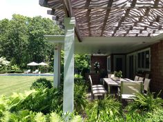 an outdoor dining table and chairs under a pergolated roof with trees in the background