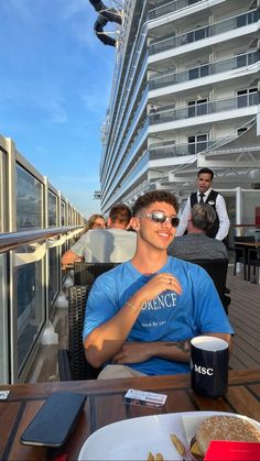 a man sitting at a table on top of a cruise ship with food and drinks