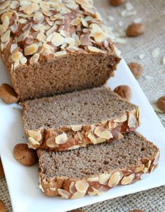 sliced loaf of bread with almonds on a white platter next to some nuts