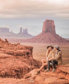 a man and woman sitting on top of a rock formation in the middle of desert