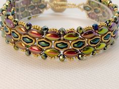 a close up of a bracelet on a white surface with gold beads and colorful stones