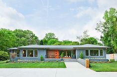 a blue house with trees in the background and grass on the front lawn, surrounded by lush greenery