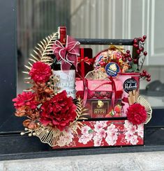 a red and gold gift basket with flowers in front of a glass door, on display