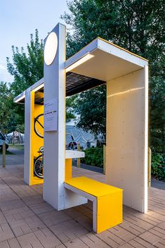 a yellow and white bus stop with a bike on it's seat area next to trees