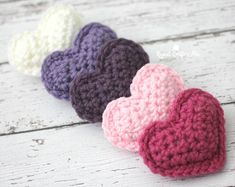 three crocheted hearts sitting on top of a white wooden table next to each other