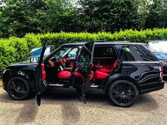 a black car with red seats is parked in front of some bushes and trees,