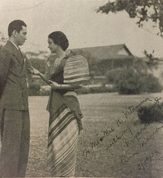 an old black and white photo of two people standing next to each other in the grass