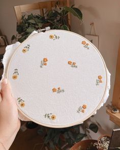 a person holding up a white embroidery project with orange flowers on it