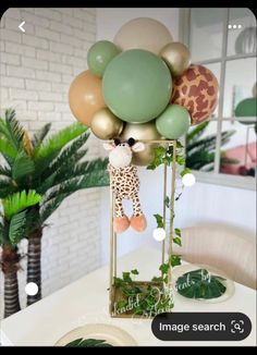 a giraffe balloon centerpiece on top of a table with greenery and balloons