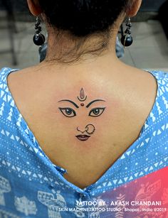 the back of a woman's neck with a face tattoo on her left side