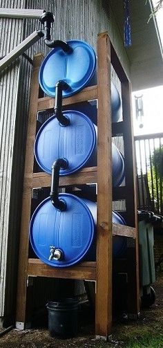 three blue barrels stacked on top of each other in front of a building with metal pipes