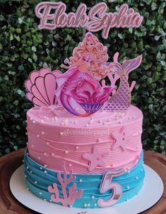 there is a pink and blue cake with a mermaid figure on the top of it