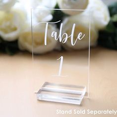 a table number is placed on top of a clear acrylic stand with flowers in the background