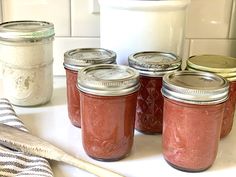 jars filled with red liquid sitting on top of a counter next to a wooden spoon