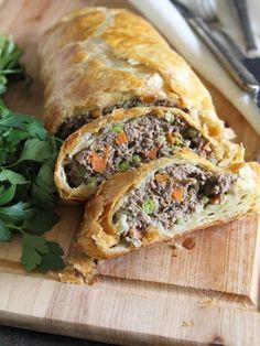 a meat and vegetable pastry cut in half on a cutting board next to parsley